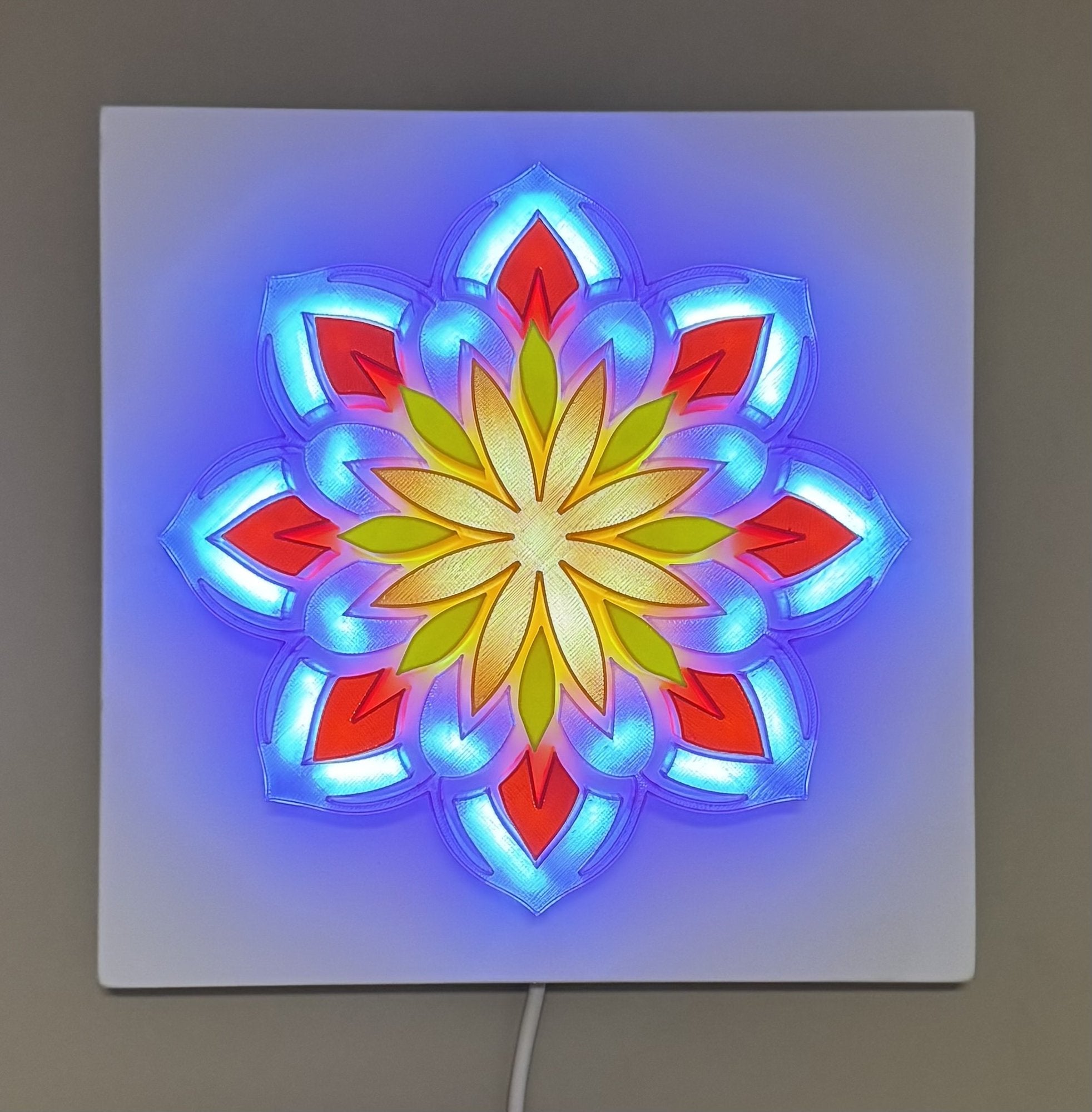 Achtzackiges Mandala-3D-Leuchtbild an der Wand: rot-blau-grün-gelbe Blütenblätter, LED-hinterleuchtet in Blau und Warmweiß, eingeschaltet